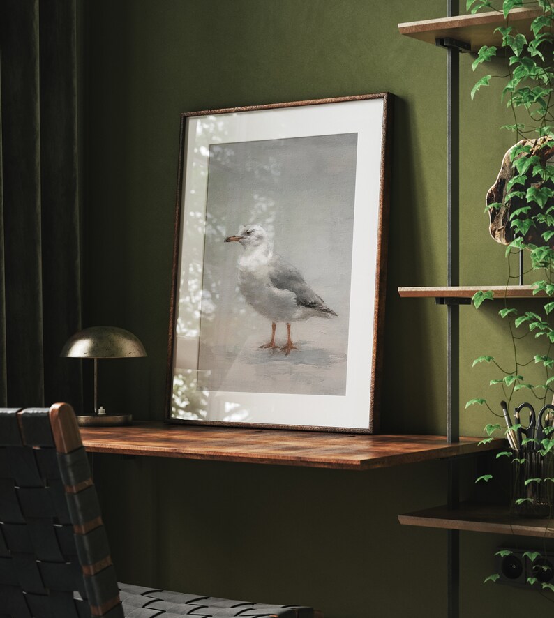 May include: A framed print of a white seagull with a gray back standing on a beach. The print is in a brown frame and is hanging on a wall.