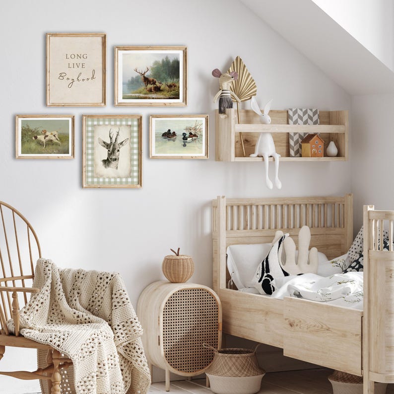 May include: A nursery room with a white wall and a wooden bed with a white and black patterned pillow. There are five framed pictures on the wall, including a deer, ducks, and a sign that says "Long Live Boyhood".