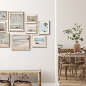 May include: A collection of framed coastal-themed artwork featuring seascapes, lighthouses, and palm trees. The artwork is displayed on a white wall above a wooden bench with woven baskets.