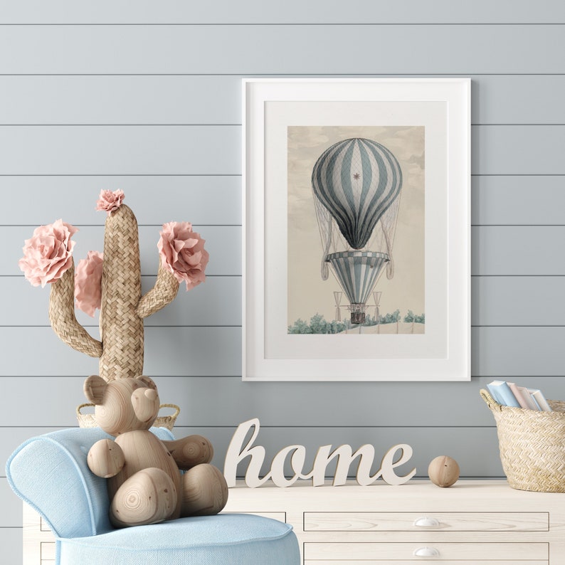 May include: A framed print of a vintage hot air balloon in shades of blue and white. The artwork is displayed on a light blue wall. A wooden cactus with pink flowers, a wooden bear, and the word "home" are also in the image.