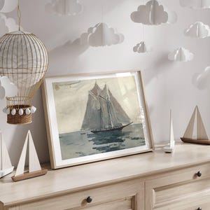 May include: A framed watercolor painting of a sailboat on the water. The sailboat has two masts and a white sail. The water is a light blue color. The painting is hanging on a wall with white paper clouds hanging from the ceiling.