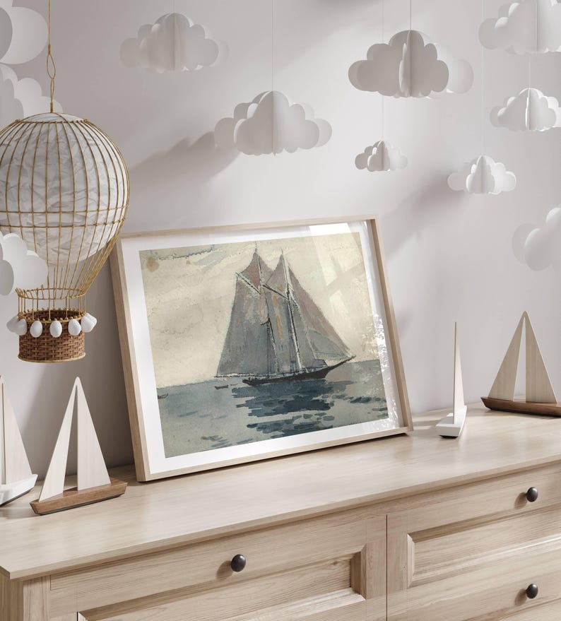 May include: A framed watercolor painting of a sailboat on the water. The sailboat has two masts and a white sail. The water is a light blue color. The painting is hanging on a wall with white paper clouds hanging from the ceiling.