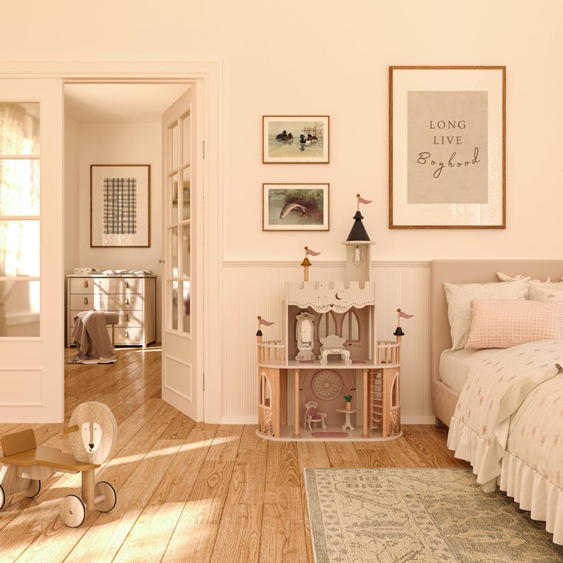 May include: A light wood toy castle with pink accents and a white roof. The castle has a mirror, a table, and a chair inside. The castle is on a light wood floor with a rug in front of it. There is a framed print on the wall that says "Long Live Boyhood".