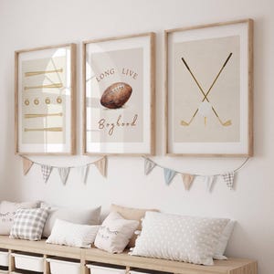 May include: Three framed prints with a sports theme. The first print features a baseball bat and ball, the second print features a football and the text "Long Live Boyhood", and the third print features two crossed golf clubs and a golf ball.