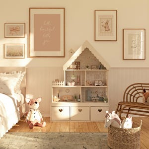 May include: A white dollhouse with a pink and white floral wallpaper interior. The dollhouse has multiple rooms and a ladder. The dollhouse is in a room with a white rug, a white bed, and a white wicker chair. There are several framed prints on the wall, including one that says "hello beautiful little you".