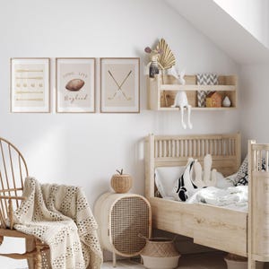 May include: A light wood framed bed with a white and black patterned pillow and a white blanket. There are three framed prints on the wall behind the bed. The prints feature a geometric pattern, a football with the text "Long Live Boyhood", and two crossed golf clubs. There is a wooden shelf with a small house and a stuffed animal on it.