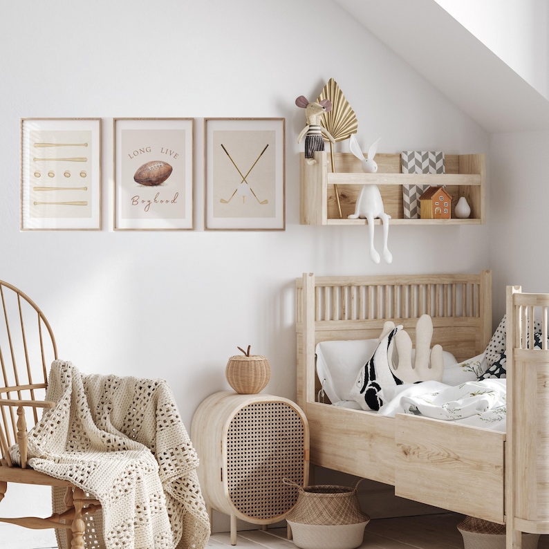 May include: A light wood framed bed with a white and black patterned pillow and a white blanket. There are three framed prints on the wall behind the bed. The prints feature a geometric pattern, a football with the text "Long Live Boyhood", and two crossed golf clubs. There is a wooden shelf with a small house and a stuffed animal on it.