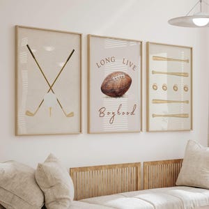 May include: Three framed prints with a sports theme. The left print features two crossed golf clubs with a golf ball. The middle print has a brown football with the text "Long Live Boyhood". The right print has a series of brown baseball bats.