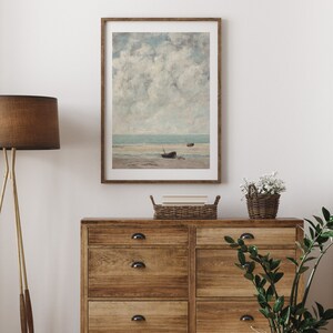 May include: A framed print of a seascape painting with a cloudy sky and two boats on the shore.