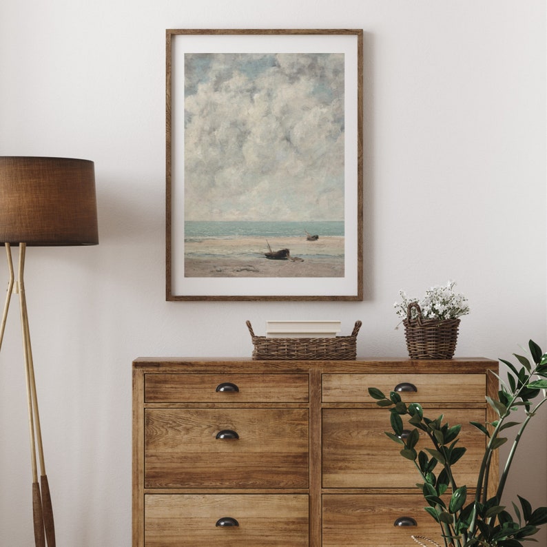 May include: A framed print of a seascape painting with a cloudy sky and two boats on the shore.