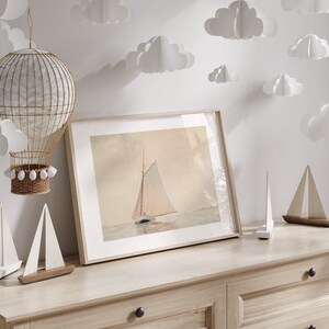 May include: A framed watercolor print of a sailboat on the water, displayed on a light wood dresser. Decorative wooden sailboat models and paper cloud cutouts are also present. A wicker hot air balloon decoration hangs from the ceiling.