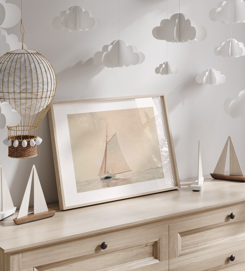 May include: A framed watercolor print of a sailboat on the water, displayed on a light wood dresser. Decorative wooden sailboat models and paper cloud cutouts are also present. A wicker hot air balloon decoration hangs from the ceiling.
