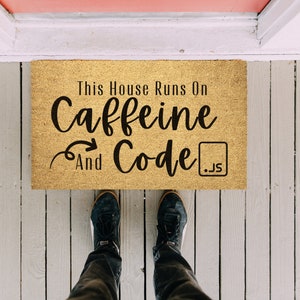 May include: A brown doormat with the text "This House Runs On Caffeine And Code .js" in black lettering.