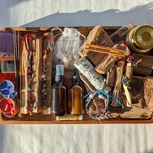Op de afbeelding: Een houten dienblad gevuld met spirituele items. Inclusief wierook, saliebundels, etherische olieflessen, kristallen, kaarsen en stukken hout. De lade is gemaakt van lichtbruin hout.