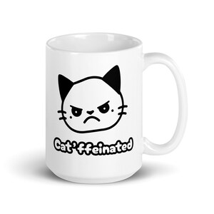 Könnte beinhalten: Weiße Keramiktasse mit einem schwarz-weißen Comic-Katzenkopf und dem Text "Cat'ffeinated".