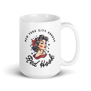 May include: White ceramic mug with a colorful illustration of a woman with a flower in her hair. The text "New York City Harbor Red Hook" is printed around the illustration.