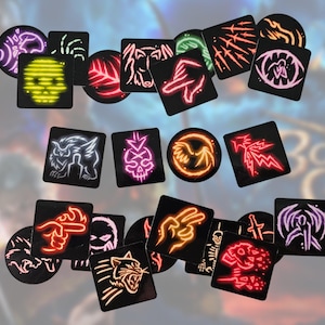 May include: A collection of black square and circular tokens featuring neon-colored graphic illustrations of various symbols, including skulls, animals, hands, and abstract shapes, arranged in a scattered layout against a blurred background.