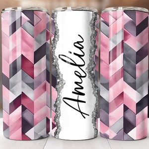 Può includere: Tre bicchieri in acciaio inossidabile con un motivo geometrico in tonalità di rosa, grigio e bianco. Il bicchiere centrale ha il nome "Amelia" scritto in corsivo nero con un bordo di glitter argentato.