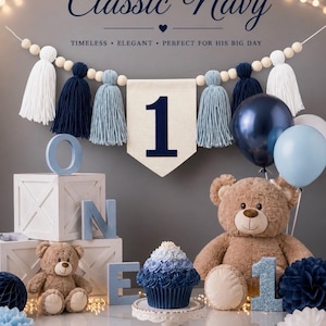 May include: A first birthday party decoration set featuring a banner with white, navy, and light blue tassels, a cream-colored pennant with the number 1, two brown teddy bears, a blue ombre cupcake, and blue and white balloons and paper pom-poms.