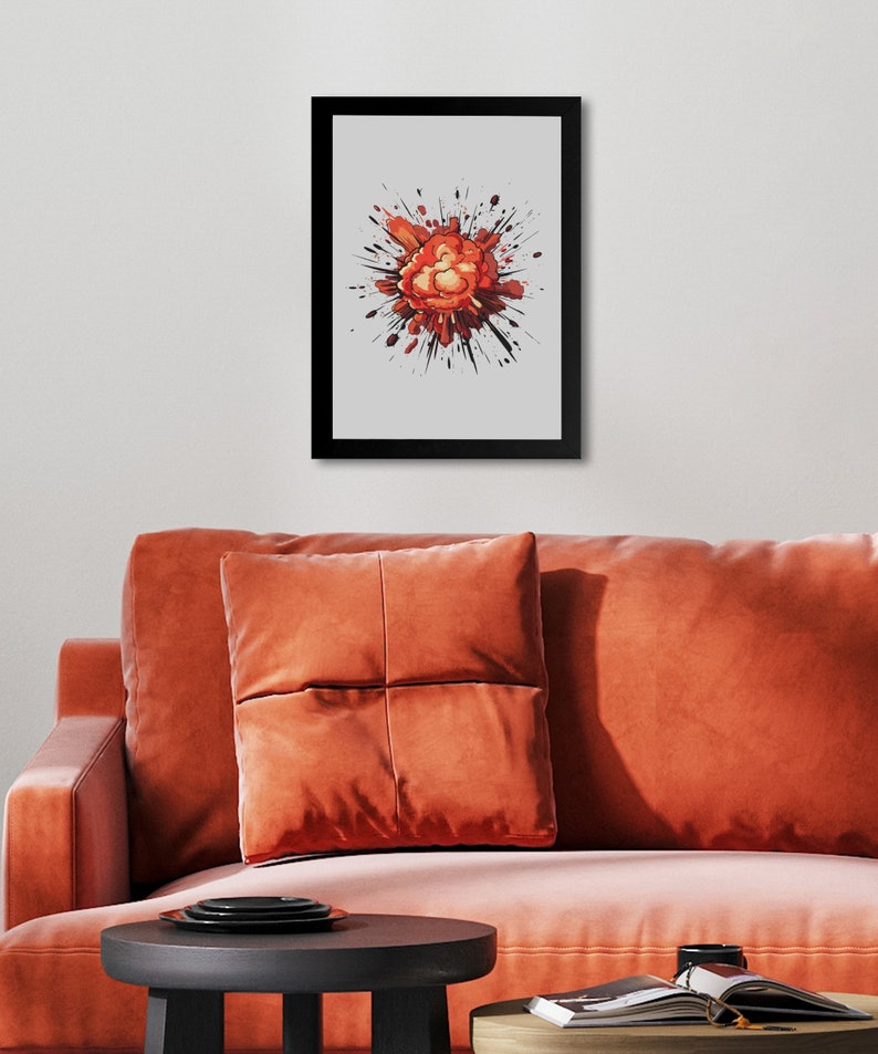 May include: Framed wall art featuring an abstract explosion graphic. The explosion is predominantly orange and red, with black splatters radiating outward against a light gray background. The artwork is presented in a black frame and displayed on an orange couch with matching throw pillows. A dark brown side table with a stack of plates and a magazine is visible in the foreground.
