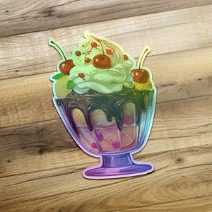 May include: A vibrant, iridescent sticker depicting a delectable sundae. The sundae is served in a clear glass dish, showcasing layers of creamy vanilla ice cream, chocolate sauce, and waffle cone pieces.  Three bright red cherries garnish the top, adding a pop of color against the light green ice cream. The sticker features a glossy, almost holographic effect, giving it a three-dimensional appearance. The overall design is whimsical and appealing, perfect for ice cream lovers and dessert enthusiasts.