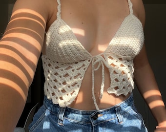 Op de afbeelding: Een wit gecrochete crop top met een strik aan de voorkant en spaghettibandjes.
