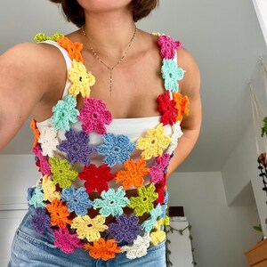 May include: A colourful crochet top with a floral design. The top is made of a variety of colours, including red, orange, yellow, green, blue, and purple. The top is sleeveless and has a loose fit.