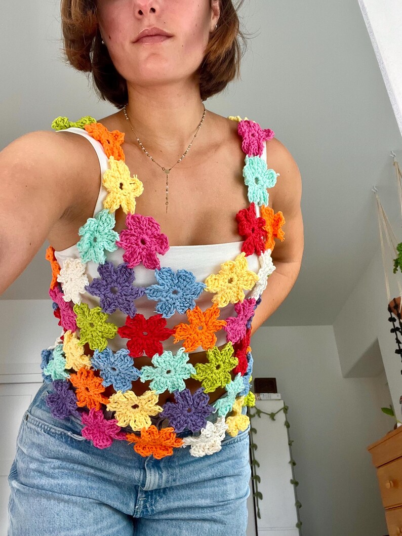 May include: A colourful crochet top with a floral design. The top is made of a variety of colours, including red, orange, yellow, green, blue, and purple. The top is sleeveless and has a loose fit.