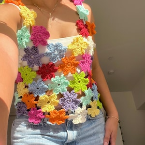 Peut inclure: Un haut en crochet coloré avec un motif floral. Le haut est fait de plusieurs couleurs vives, dont le rose, le jaune, le vert, le bleu et l'orange. Le haut est sans manches et a un col rond. Le haut est porté sur un débardeur blanc.
