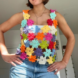 May include: A colourful crochet top with a floral design. The top is made of a variety of colours, including pink, blue, green, yellow, and orange. The top is sleeveless and has a loose fit.
