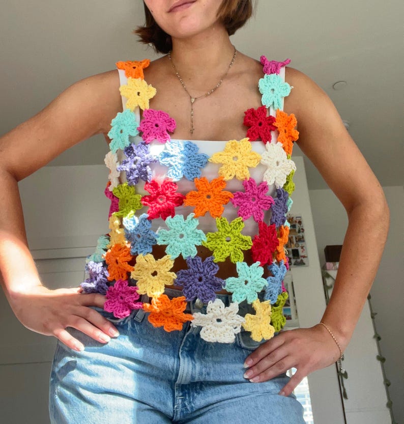 May include: A colourful crochet top with a floral design. The top is made of a variety of colours, including pink, blue, green, yellow, and orange. The top is sleeveless and has a loose fit.