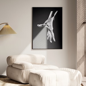 Peut inclure: Une impression d'art encadrée noire avec un dessin au trait blanc détaillé d'une main tendue. L'œuvre est affichée sur un mur au-dessus d'un fauteuil et d'un pouf rembourrés beiges. Un lampadaire doré avec un abat-jour plissé est à gauche.