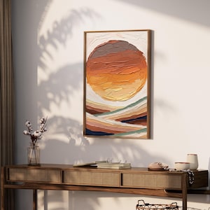 Può includere: Dipinto astratto incorniciato con un design strutturato a strati. L'opera raffigura un grande sole arancione su uno sfondo di colline a tinte terrose. Il dipinto è appeso a una parete bianca, sopra una consolle in legno.