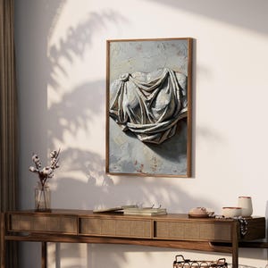 Op de afbeelding: Een rechthoekig ingelijst wandkunstwerk met een getextureerd olieverfschilderij van een klassiek gedrapeerd torsobeeld. Het kunstwerk gebruikt grijze, witte en beige tinten met dikke impasto penseelstreken voor diepte en schaduw.
