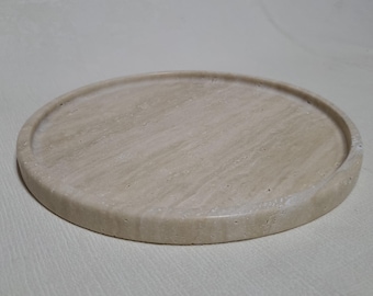 May include: A round, beige travertine serving tray with a slightly raised edge.