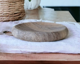 May include: A rustic wooden serving tray with a natural brown finish sits on a white linen tablecloth. The tray is oval shaped and has a slightly raised edge.