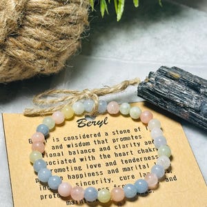 May include: A light blue, pink and yellow beaded bracelet with a brown card that reads "Beryl is considered a stone of love and wisdom that promotes emotional balance and clarity and associated with the heart chakra, promoting love and tenderness, happiness and marital sincerity, cure laziness, and protects from stress."