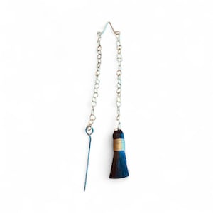 May include: A single earring with a silver chain and a dark blue tassel. The tassel is wrapped with gold-colored wire. The earring has a long, thin, silver post.