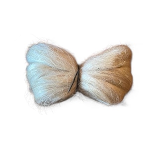 May include: A light beige, butterfly-shaped object made of soft, fibrous material. The two halves are joined in the middle with a thin, dark wire. The object has a fluffy, textured appearance, suggesting it is made of natural fibers.
