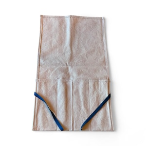 May include: A beige tool roll with multiple pockets and blue ties. The roll is made of a textured material and is designed to hold various tools. The pockets are visible at the bottom of the roll, and the blue ties are used to secure the roll.
