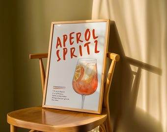 Pode incluir: Uma impressão emoldurada em uma cadeira de madeira apresenta as palavras "APEROL SPRITZ" em letras vermelhas. A impressão inclui uma ilustração em aquarela do coquetel com fatias de laranja e gelo. Os ingredientes estão listados abaixo.