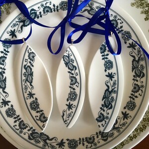 May include: Three white ceramic ornaments with a blue and white floral design. The ornaments are hanging from blue ribbon on a white plate with a blue and white floral design.