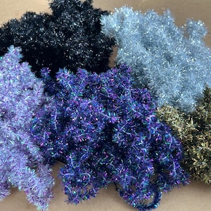 Könnte beinhalten: Eine Auswahl an farbenfrohem Lametta in verschiedenen Farbtönen, darunter Schwarz, Silber, Lila, Blau und Gold. Das Lametta hat ein glänzendes, strukturiertes Aussehen, ideal zum Basteln oder für festliche Dekorationen.