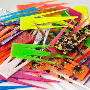 Könnte beinhalten: Eine Auswahl an bunten Kunststofffischködern in verschiedenen Formen und Größen. Einige der Köder sind mit Glitzer und Mustern verziert.