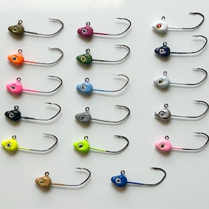 Könnte beinhalten: Sortiment von 15 Jigköpfen in verschiedenen Farben, darunter Grün, Blau, Pink, Gelb, Schwarz, Weiß und Braun. Jeder Jigkopf hat einen Haken und eine kleine Öse.