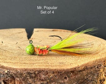 May include: A set of four green, orange, and yellow fishing lures with feathers. The lures are called "Mr. Popular" and are displayed on a wooden surface.