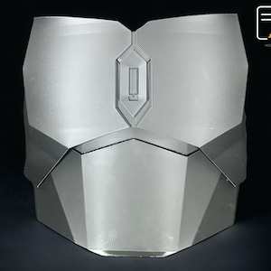 May include: A silver-colored, 3D printed chest piece with a geometric design. The chest piece has a raised, rectangular panel in the center with a small, rectangular opening.