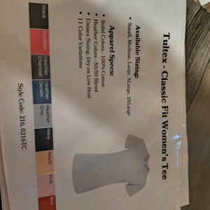 以下が含まれることがあります： 白紙に表示された、ライトグレーのTultex Classic Fit Women's Tee。利用可能なサイズ、アパレル仕様、色のバリエーションも記載されています。このシャツは半袖、クルーネックです。