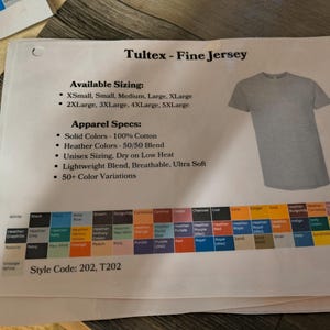 以下が含まれることがあります： Tultex Fine Jersey Tシャツに関する情報が印刷されたシート。利用可能なサイズ、アパレル仕様、カラーチャートが含まれています。グレーのTシャツが示されています。スタイルコードは202、T202です。