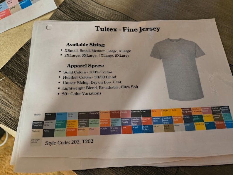 以下が含まれることがあります： Tultex Fine Jersey Tシャツに関する情報が印刷されたシート。利用可能なサイズ、アパレル仕様、カラーチャートが含まれています。グレーのTシャツが示されています。スタイルコードは202、T202です。